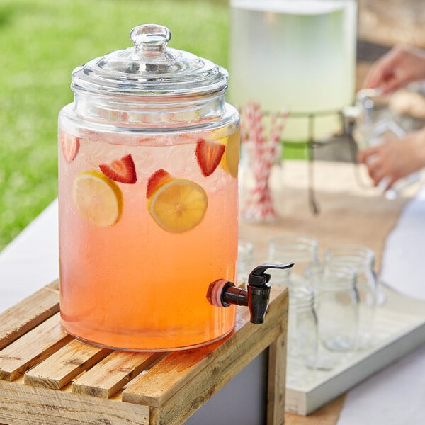 An Acopa glass beverage dispenser filled with pink drink with strawberries and lemons.