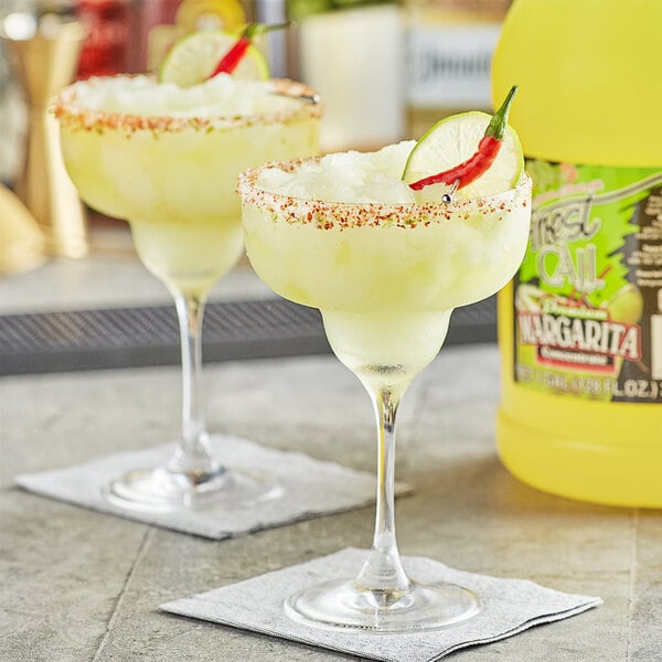 Two glasses of Finest Call margaritas garnished with lime and chili peppers on a table.