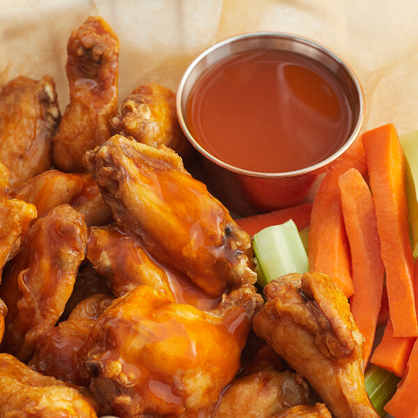 A plate of chicken wings with carrots and a bowl of Crystal Buffalo Wing Sauce.