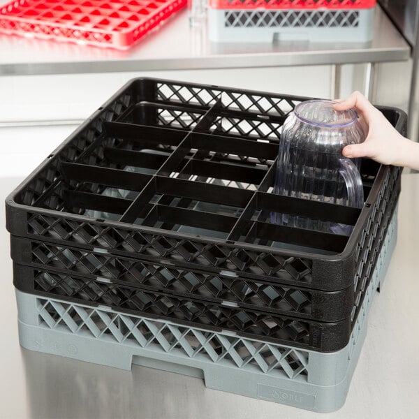 A hand holding a glass in a black and grey Noble Products glass rack with black extenders.