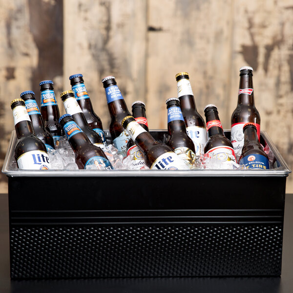 An American Metalcraft black hammered rectangular beverage tub filled with beer bottles on a table.