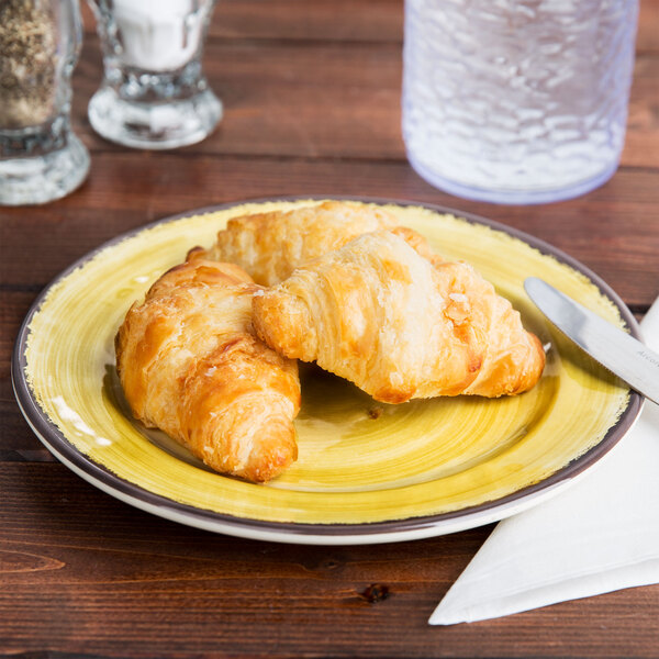 A Carlisle amber melamine bread and butter plate with two croissants and a knife on it.