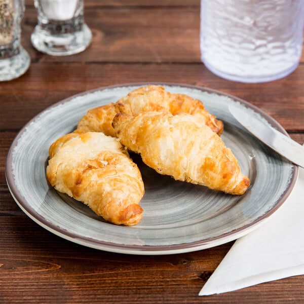 A Carlisle Mingle smoke melamine bread and butter plate with croissants on a wooden table.