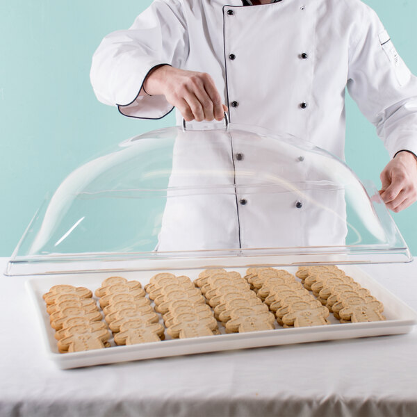 A chef using a Cambro clear dome display cover to cover a tray of cookies.