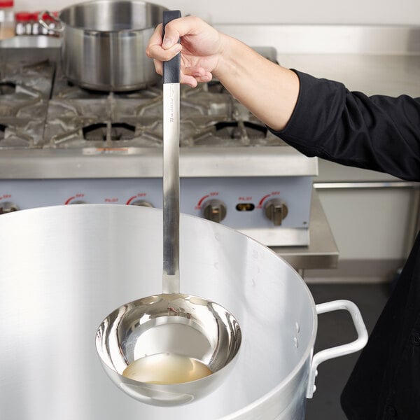 A woman using a Vollrath stainless steel ladle with a black handle to pour liquid into a large pot.