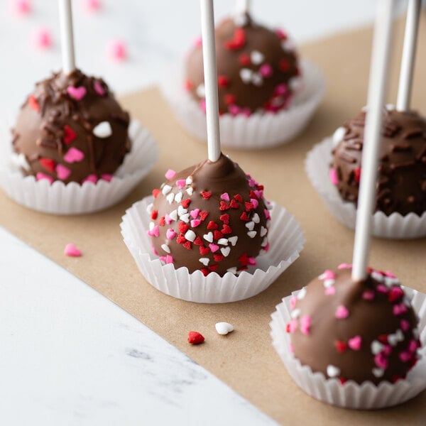 A group of chocolate cake pops in white fluted mini baking cups with hearts sprinkles.