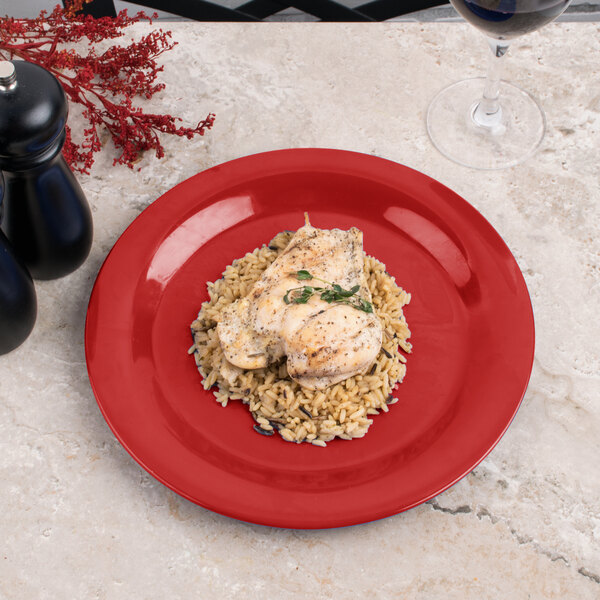 A red Carlisle Sierrus melamine plate with chicken and rice on a table.