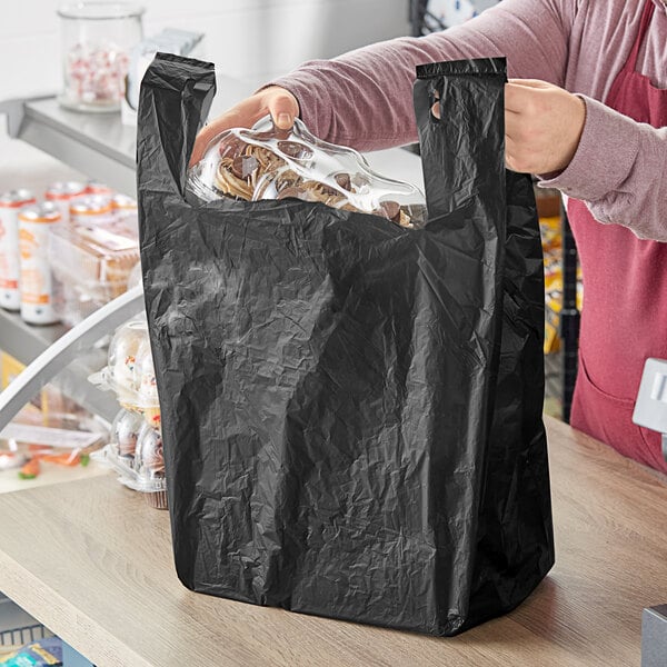 A person holding a black plastic bag with food inside.