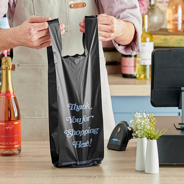 A man holding a black plastic bag with blue writing that says "Thank You" containing a bottle.