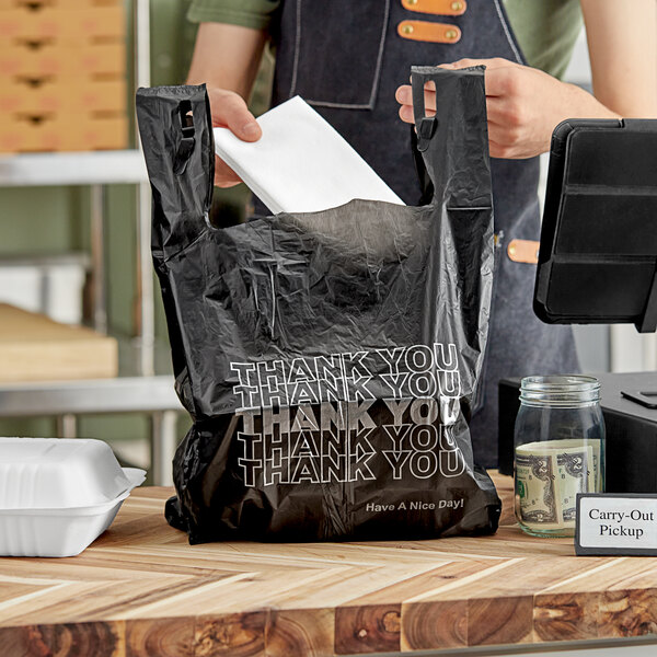 A person putting a white envelope in a black plastic "Thank You" bag.