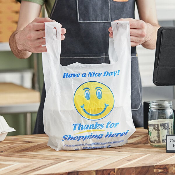 A person holding a white plastic t-shirt bag with a happy face on it.