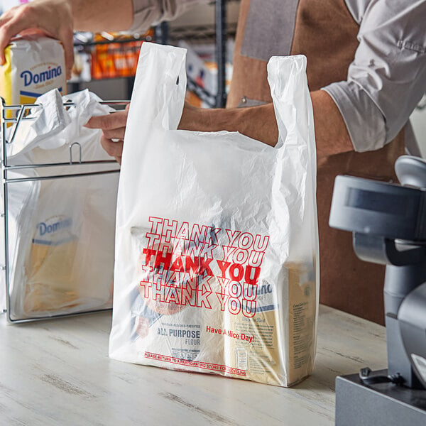 A person holding a white "Thank You" plastic bag.