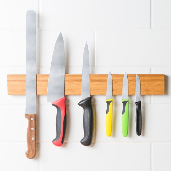 A Mercer Culinary bamboo magnetic knife holder with knives on it.