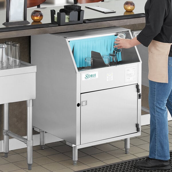 A woman standing at a counter using a Noble Warewashing electric carousel glass washer.