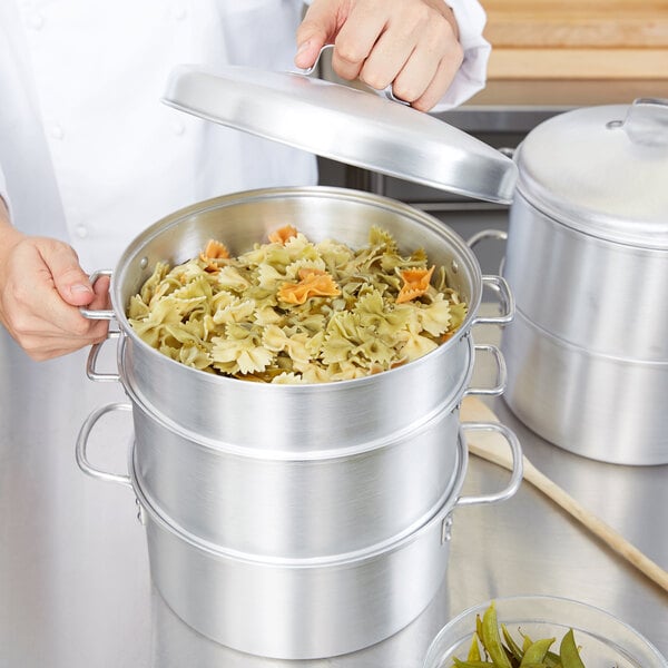 A person using the Vollrath 3-Tier Vegetable Steamer Set to cook vegetables.