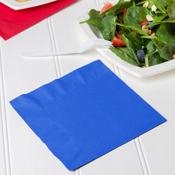 A Creative Converting cobalt blue luncheon napkin with a plate of salad and a fork.