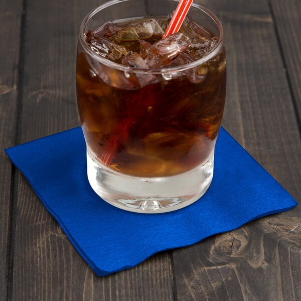 A glass with ice and a straw on a blue Creative Converting beverage napkin.