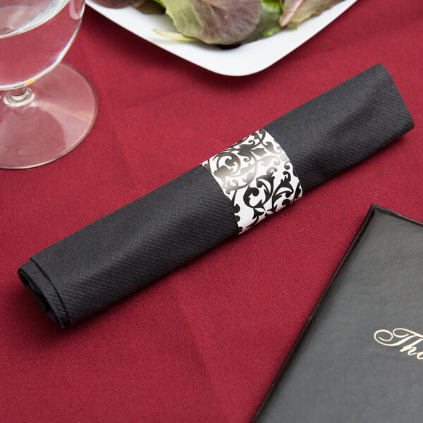 A black napkin with a silver band on it next to clear plastic cutlery.