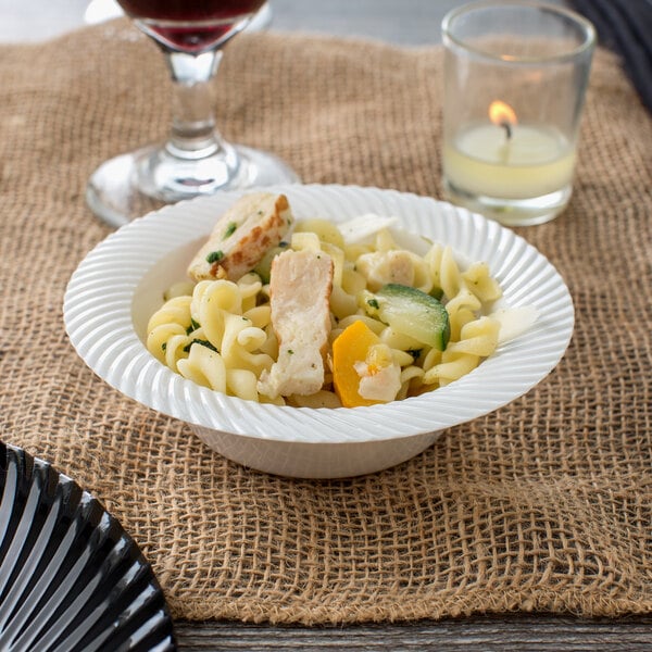 A Visions plastic bowl filled with pasta and meat and vegetables on a table with a candle and wine.