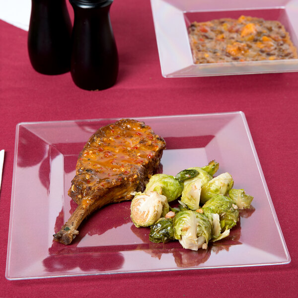 A Visions Florence clear plastic plate with meat and brussels sprouts on a table.