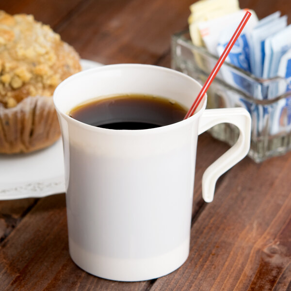 A Visions ivory plastic coffee mug filled with coffee and a straw next to a muffin.