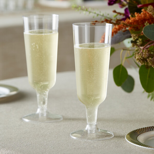 Two Visions clear plastic champagne flutes on a table with a bouquet of flowers.