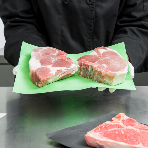 A person holding a piece of meat on a green steak paper.