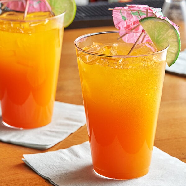 Two Choice clear disposable plastic tumblers filled with orange liquid and ice, garnished with lime slices.