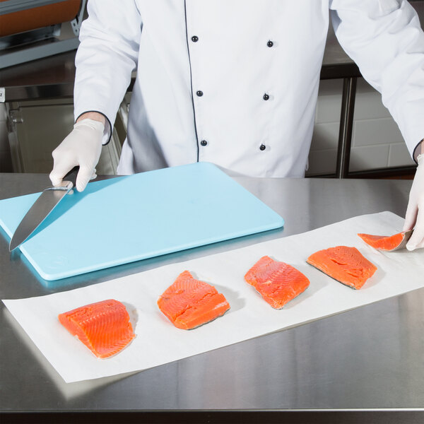 A chef cutting raw salmon on a white Choice steak paper-covered surface.
