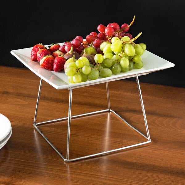 A table with an Acopa Square China Plate and fruit on it displayed on a stainless steel stand.