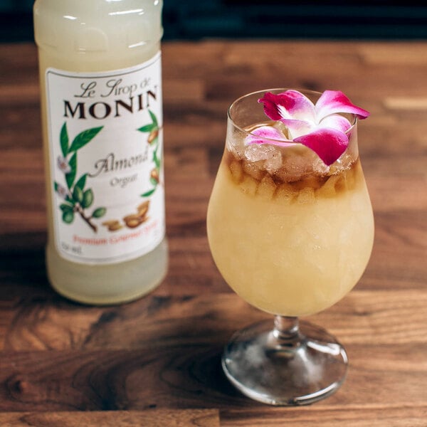 A glass of Monin Almond flavored liquid with a flower on top next to a bottle.