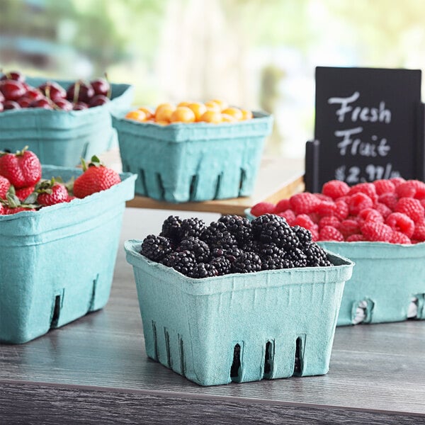 A table with several green baskets of berries inside blue containers.