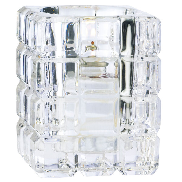 A close-up of a clear glass Sterno Krystle square candle holder with a candle inside.
