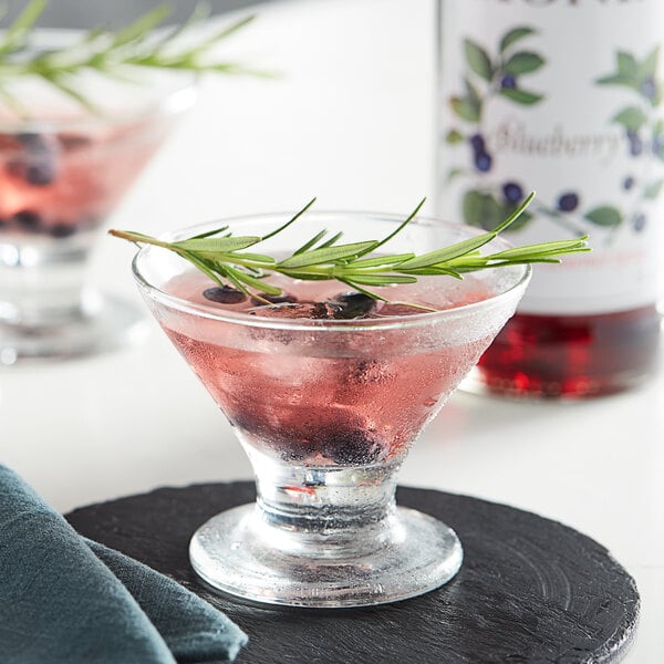 A glass of Monin blueberry flavored drink with a sprig of rosemary.