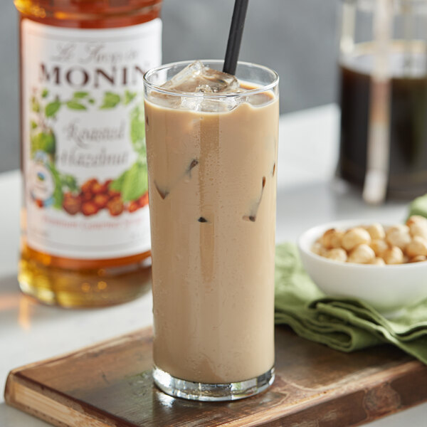 A glass of iced coffee with Monin Roasted Hazelnut Flavoring Syrup and a black straw.