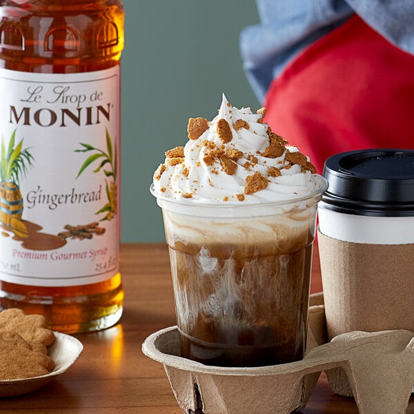 A cup of coffee with Monin Gingerbread Flavoring Syrup on a table with cookies.