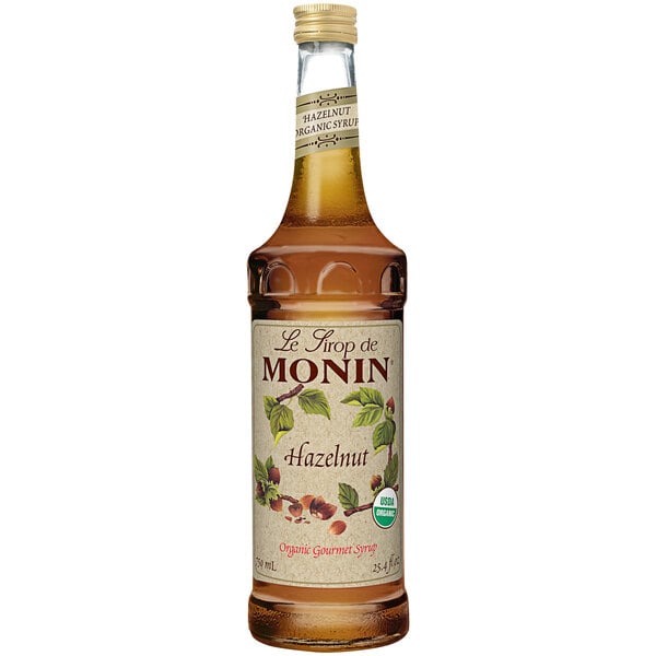 A Monin Organic Hazelnut Flavoring Syrup bottle with a label filled with brown liquid.