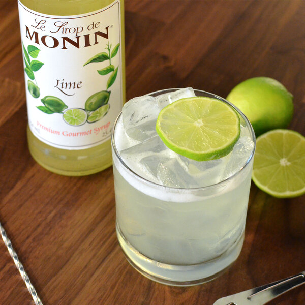A glass of liquid with ice and a lime wedge made with Monin Premium Lime Syrup.