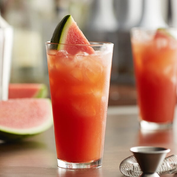 A glass of Monin watermelon puree with a slice of watermelon on the rim.
