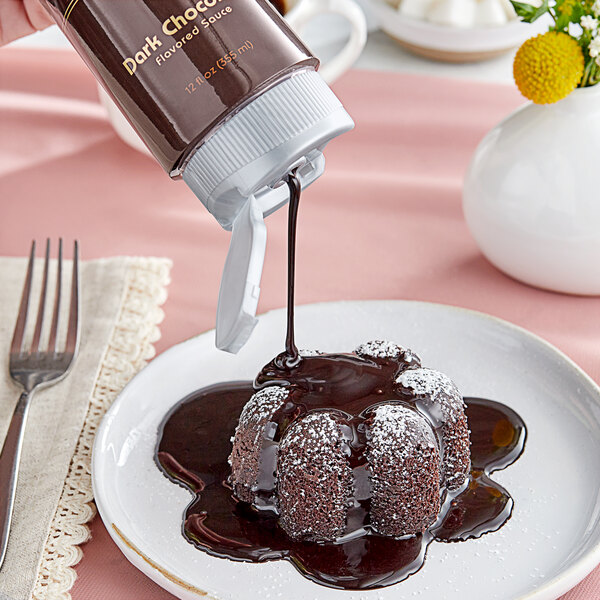 A person pouring Monin Dark Chocolate Flavoring Sauce on a chocolate cake.
