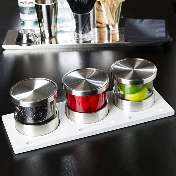 A Cal-Mil wooden display with three glass jars filled with fruit and stainless steel lids on a counter.