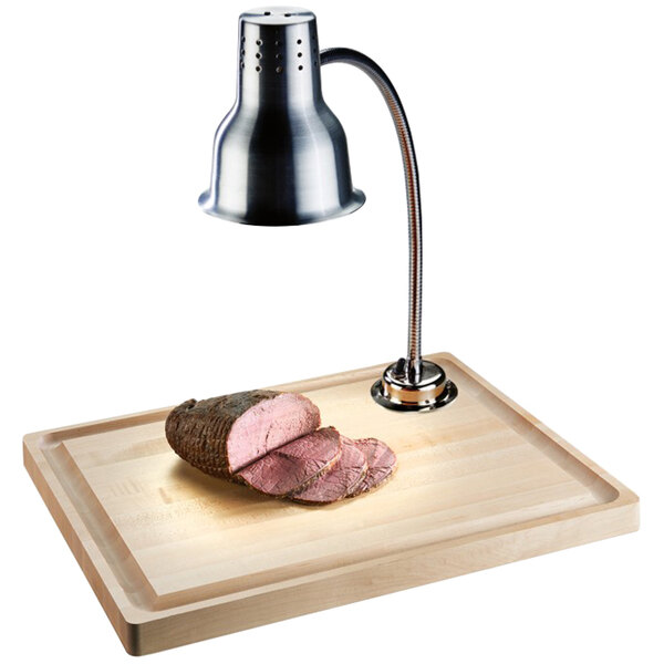 A piece of meat on a Cal-Mil maple carving station with a lamp above it.