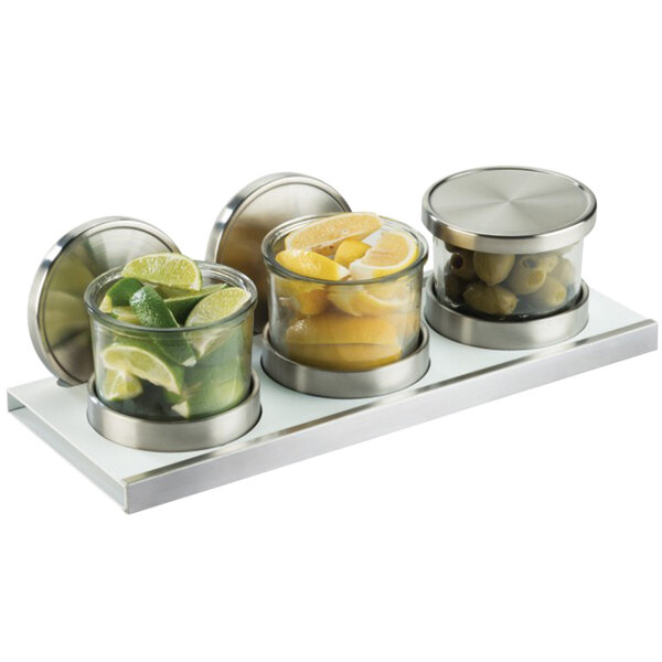 Three glass jars with lemons, limes, and green olives in a tray with a solid lid.