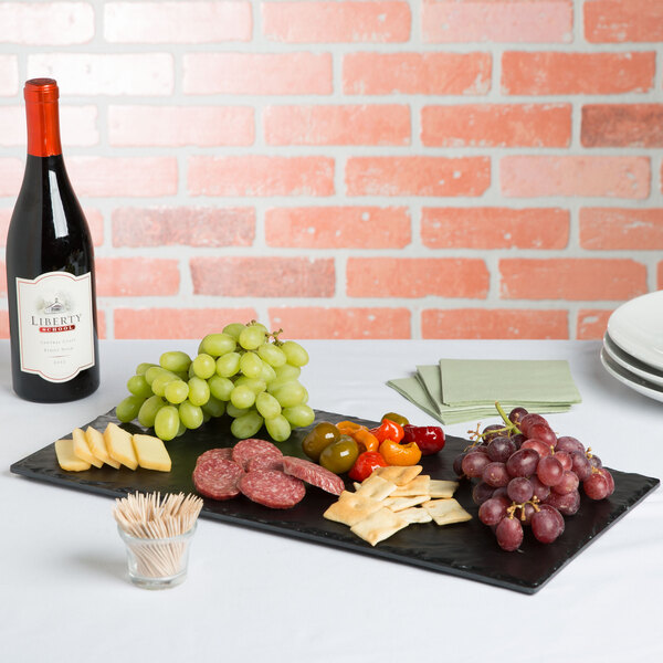 A rectangular melamine serving platter with cheese, crackers, grapes, and a bottle of wine on it.