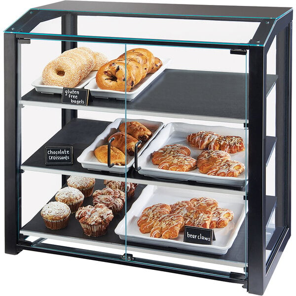 A Cal-Mil black bakery display case on a counter filled with bagels, donuts, and muffins.