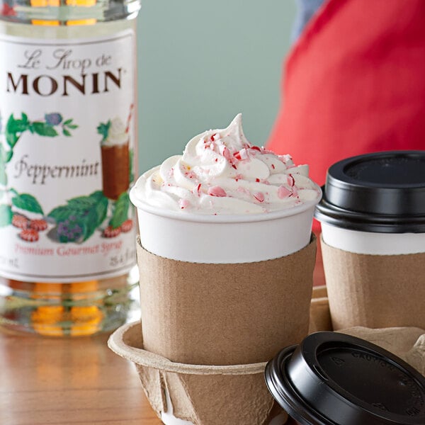 A cup of coffee and a cup of hot chocolate with Monin Premium Peppermint Flavoring Syrup on a counter.