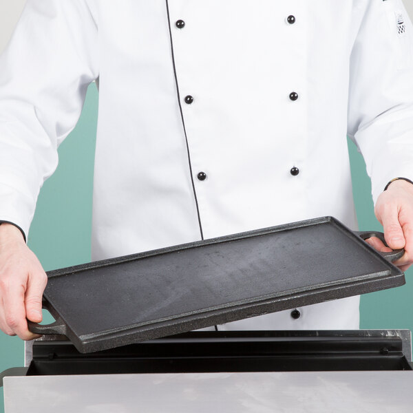 A chef holding a Cal-Mil rectangular black metal cast iron griddle pan with handles.
