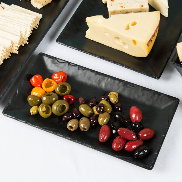 A variety of cheese, olives, and crackers on a Cal-Mil faux slate platter on a table in a catering event.