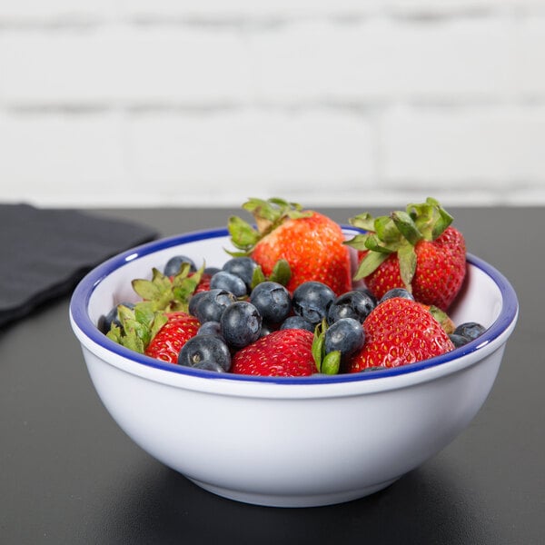 A Cal-Mil white melamine bowl with blue rim filled with strawberries and blueberries.