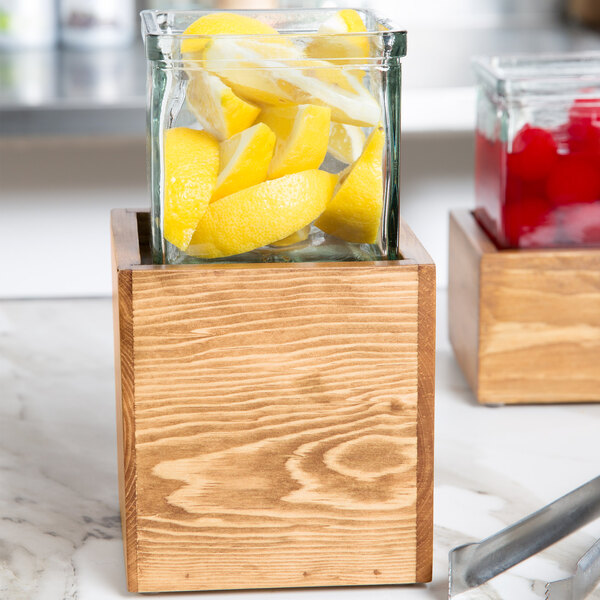 A glass jar filled with lemon slices in a wooden container.